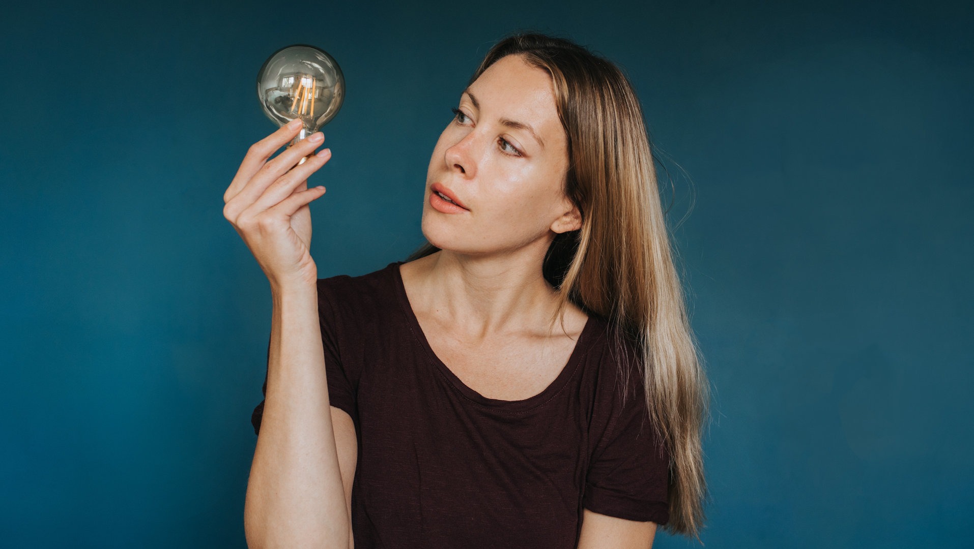Une femme tient une ampoule devant un fond bleu et a l’air méditative.