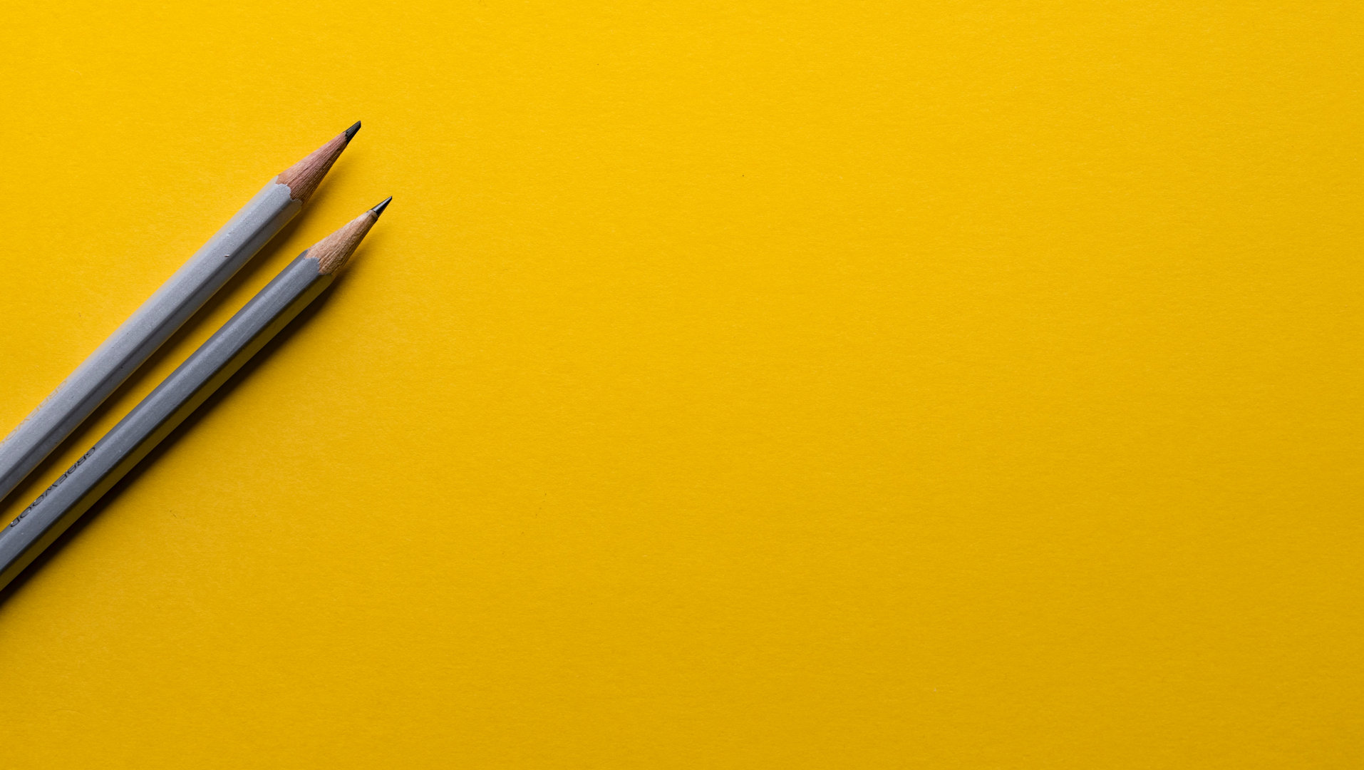 Deux crayons gris sont disposés en diagonale sur un fond jaune.